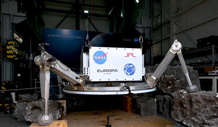 The proposed lander is seen inside a hanger with its legs outspread on artificial rocks.