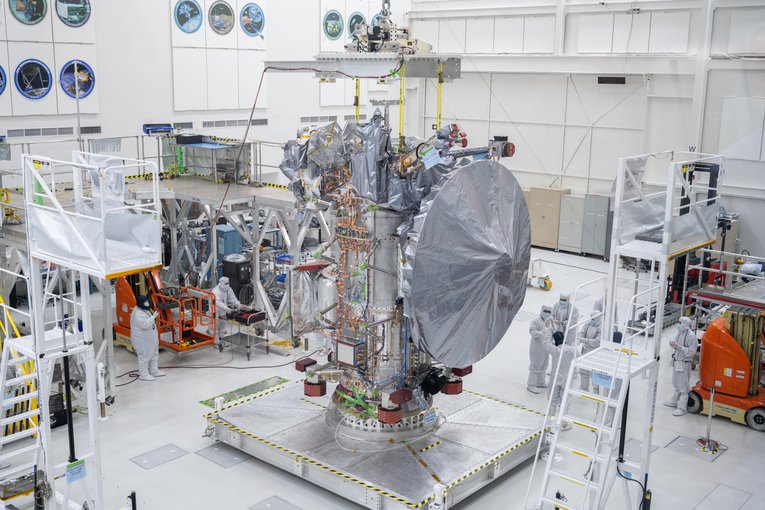 Europa Clipper's high gain antenna, which is taller than the nearby workers, is covered in a protective shroud as it sits on a platform at NASA's Jet Propulsion Laboratory.