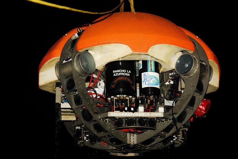 DEPTHX is a cicrular robotic vessel seen from a low angle. The dome-like top is bright orange. Four arching metal bars encase instruments beneath the vehicle.