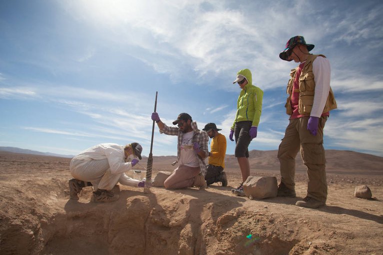 Mary Beth Wilhelm (left, in white cleanroom suit) carefully samples ground-truth material obtained from the 2.2 meter depth science excavation pit, assisted by Jonathan Araya (Univ. de Antofagasta) and watched by ARADS co-investigators Miriam Villadangos, and the SOLID instrument lead, Victor Parro, both of Centro de Astrobiologia (CAB), Spain. Credits: NASA