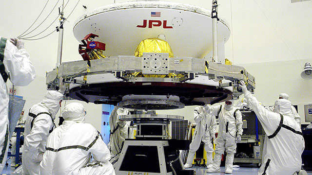 In the Payload Hazardous Servicing Facility, workers prepare to lift the Mars Exploration Rover-1 (MER-B) onto a spin table during preflight processing of the spacecraft. Researchers at Cal Poly offer the first biochemical evidence explaining the reason why contamination persist after use of the cleaning facility. Image source: NASA/JPL/KSC Image credit: None