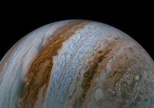 A detailed image of Half of Jupiter against the jet black background of space. In the image the planet looks tilted on it's side, with the white and orange stripes of clouds running vertically. Half the globe is visible and rests at the base of the frame.