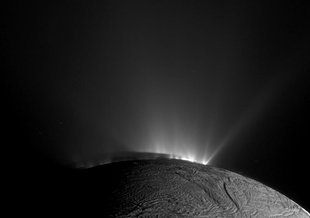 Sprays from fissures are seen as bursts of light erupting from Enceladus. Part of the moon is visible at the bottom of the frame as an arched body with a cracked surface.