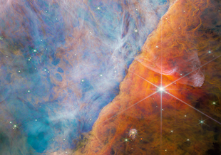 The nebula looks like colorful clouds of dust that fill the entire frame. Toward the top left the clouds appear as a mixture of pink and blue. The bottom right is filled with orange clouds. Bright pinpoints and flares of light from stars peak through.