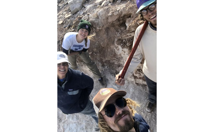 Four researchers stand in an excavation pit looking up at the camera.