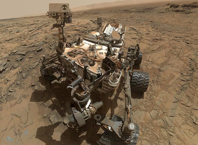 In this image, composed of dozens of photographs, the Mars Curiosity rover is pictured next to a drill hole it has made in the martian surface, seen in the lower left-hand corner.