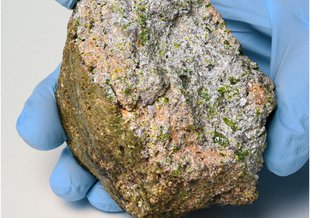 Photograph of the main mass of NWA 11119 that was found in Mauritania in December 2016. The rock has a light-green fusion crust, and the broken interior shows light-green and gray-colored crystals.
