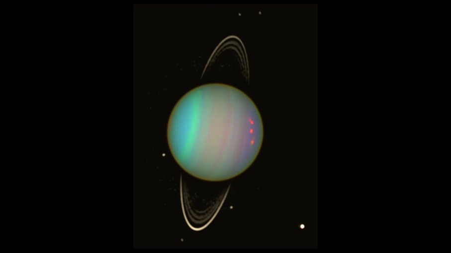 Uranus sits in the middle of the frame with greenish-blue hues. Dots of light in the blackness around the planet mark its moons. Uranus' ring can be seen as a line running north to south.