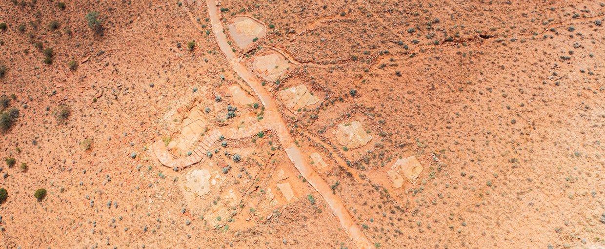 A overhead view of the fossil site at Nilpena from an angle where hills and sky are visible. tracks and paths can be seen on bare earth with some small scrubs visible as the only plant life.