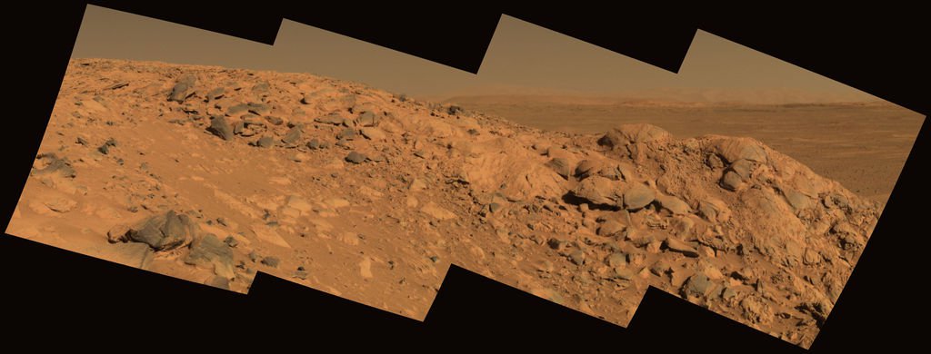 Perched Above Gusev Crater. This approximate true-color image taken by the Mars Exploration Rover Spirit shows a rock outcrop dubbed "Longhorn," and behind it, the sweeping plains of Gusev Crater. On the horizon, the rim of Gusev Crater is clearly visible. The view is to the south of the rover's current position. The image consists of four frames taken by the 750-, 530- and 430-nanometer filters of Spirit's panoramic camera on sol 210 (August 5, 2004).