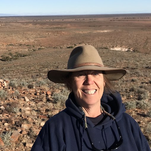 Mary Droser smiling at the camera at the Nilpena site in South Australia. She wears a wide brimmed hat and a blue coat.