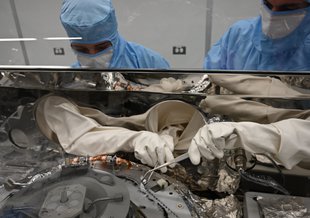 Astromaterials processors Mari Montoya, left, and Curtis Calva, right, use tools to collect asteroid particles from the base of the OSIRIS-REx science canister. NASA has already collected 70.3 grams of material with more still inside the canister.