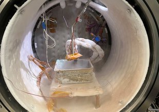 The chamber is a large circular tube on its side. Suspended in the center on a platform is a tinfoil tray. Wires run to a sensor above the tray, some coated in frost. The inside of the tube is also frost-covered much like a freezer.