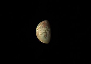 Io sits in the center of the image on a black, starless background. The moon is yellow and orange with some surface features visible with the right half of the moon shrouded in darkness.