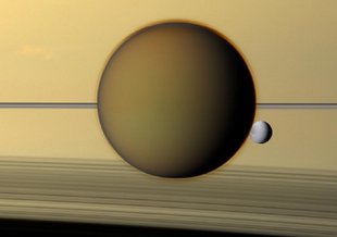 Saturn's third-largest moon Dione can be seen through the haze of its largest moon, Titan, in this view of the two posing before the planet and its rings from NASA's Cassini spacecraft.