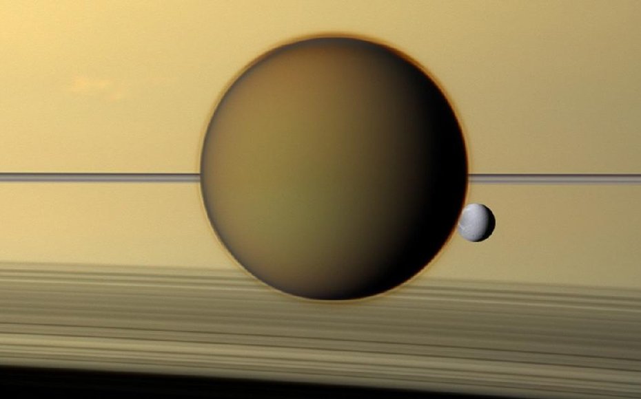 Saturn's third-largest moon Dione can be seen through the haze of its largest moon, Titan, in this view of the two posing before the planet and its rings from NASA's Cassini spacecraft.