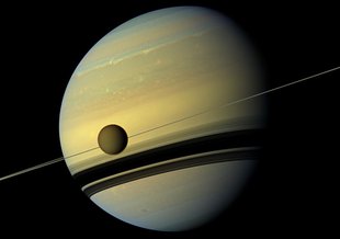Larger than the planet Mercury, Huge moon Titan is seen here as it orbits Saturn. Below Titan are the shadows cast by Saturn's rings. This natural color view was created by combining six images captured by NASA's Cassini spacecraft on May 6, 2012.
