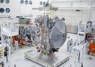 Europa Clipper's high gain antenna, which is taller than the nearby workers, is covered in a protective shroud as it sits on a platform at NASA's Jet Propulsion Laboratory.