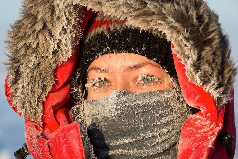 Britney's eyes are the center of focus as she looks at the camera in a closeup. Her mouth is covered by a scarf and she wears a heavy coat with the lined hood pulled up. She is covered in frost.