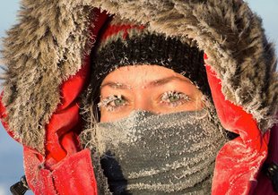 Britney's eyes are the center of focus as she looks at the camera in a closeup. Her mouth is covered by a scarf and she wears a heavy coat with the lined hood pulled up. She is covered in frost.
