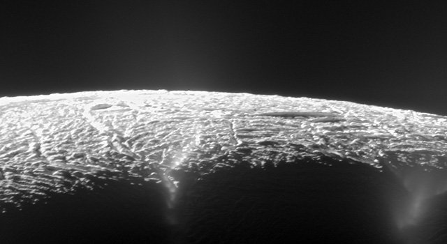 The cracked, icy surface of Enceladus is seen at the bottom of the frame against the black background of space. The picture is from far enough away that the curvature of the moon's surface is apparent.