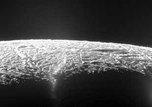 The cracked, icy surface of Enceladus is seen at the bottom of the frame against the black background of space. The picture is from far enough away that the curvature of the moon's surface is apparent.