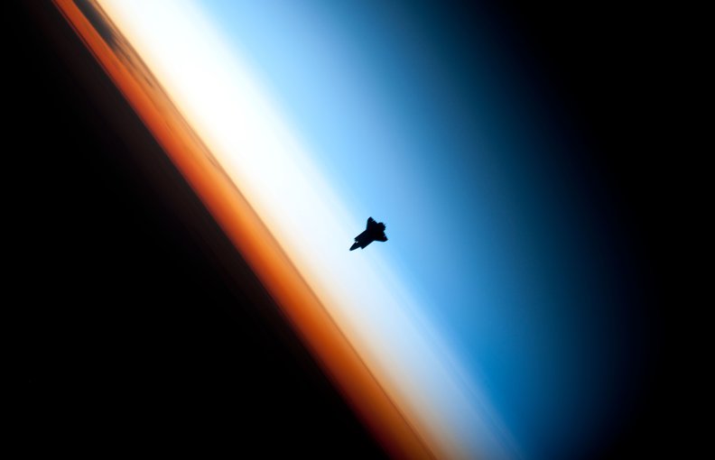 The space shuttle Endeavour hangs against Earth’s atmosphere. The stratosphere is represented by the whitish layer.