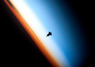 The space shuttle Endeavour hangs against Earth’s atmosphere. The stratosphere is represented by the whitish layer.
