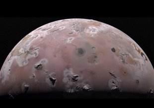 The northern half of Io is visible as half a disk against a black background. The moon is somewhat pinkish and the peaks of mountains are seen at the bottom of the image (from above) running across the moon's middle with other pockmarks and craters.