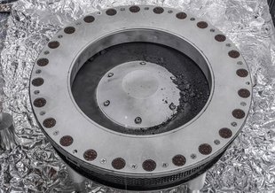 The circular sample collector fills the center of the frame and sits on what looks like aluminum foil. It's outer ring has rivet holes. A trough inside the inner ring is full of sample material.