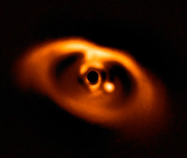 The first clear image of a planet caught while being formed, around the dwarf star PDS 70. The planet is visible as a bright point to the right of center. The star at the center is blacked out by a coronagraph mask that blocks its blinding light.