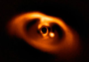 The first clear image of a planet caught while being formed, around the dwarf star PDS 70. The planet is visible as a bright point to the right of center. The star at the center is blacked out by a coronagraph mask that blocks its blinding light.