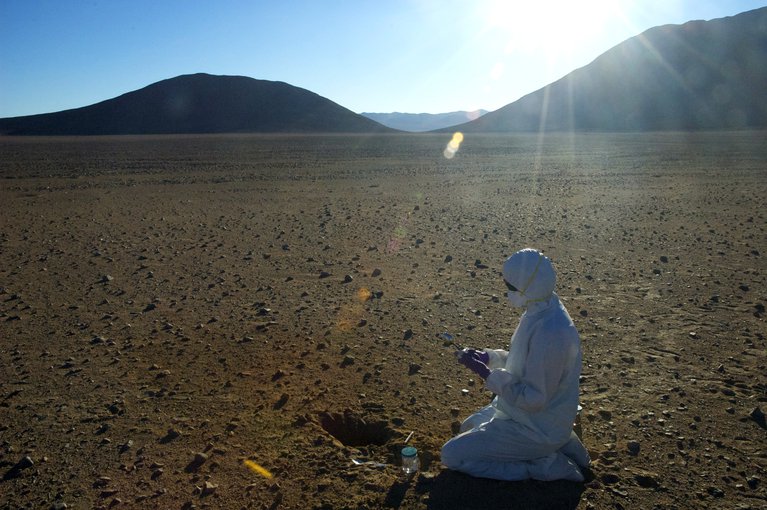 The Atacama desert is one of the driest places on Earth, making it a good Mars analogy. A scientist searching for signs of life (“biomarkers”) in the soil must use clean suits, gloves, masks, goggles, and sterile tools to make sure no contamination ends up in the sample.  Image credit: Alfonso Davila/SETI Institute