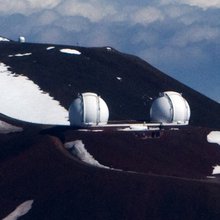 An arial shot of the twin Keck telescopes on a bright winter day on the snow capped summit of Mauna Kea.