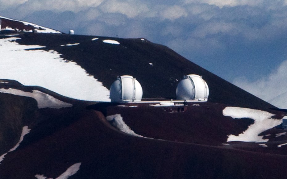 An arial shot of the twin Keck telescopes on a bright winter day on the snow capped summit of Mauna Kea.